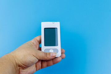 Digital glucometer in female hand over a pastel blue background. Diabetes concept
