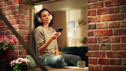Beautiful Smiling Brazilian Woman Sitting on Windowsill Using Smartphone Apps, Browsing Internet, Searching Interesting, Dating Service, Smiling Happily. Shot Through Sunny Apartment Window.
