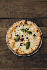 italian pizza with burnt sides on a wooden background top view. four cheese pizza with cream sauce and garnished with basil leaves, pine nuts and balsamic cream. sliced pizza close-up