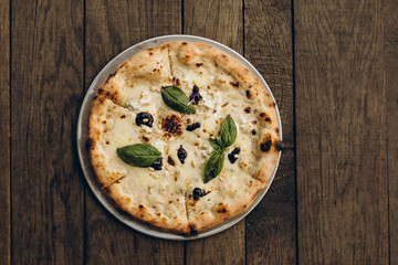 italian pizza with burnt sides on a wooden background top view. four cheese pizza with cream sauce and garnished with basil leaves, pine nuts and balsamic cream. sliced pizza close-up	