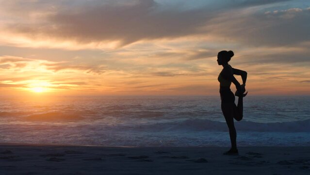 Active athlete silhouette keeping fit for healthy lifestyle, doing stretch exercises after running on beach front of ocean. Sporty female jogger warm up before workout with view of sea and sunset.