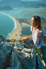 Young woman hiker rock climber climbs up on cliff on mountain over beautiful sea coast in Turkey. active lifestyle, healthy leisure, outdoors activity by traveling in Turkey at summer