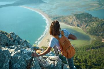 Back view tourist woman climbing up on rock, hiking in mountains over beautiful seashore in Turkey, enjoying nature view