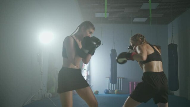 Combat sparring of two females fighters, training in the boxing gym, females train defence and series of punches on a battle, woman power.