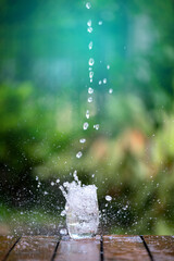 Drink water pouring in to glass over sunlight and natural green background.Water splash  in glass Select focus blurred background.