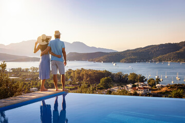 Loving couple on vacation time enjoys the summer sunset over the Aegean Sea by the swimming pool,...