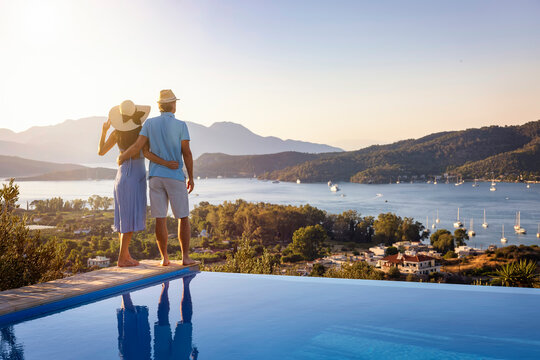 Loving couple on vacation time enjoys the summer sunset over the Aegean Sea by the swimming pool, Greece