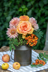 Arrangement mit Blumenstrauß mit orange Rose, Dahlien und Ebereschen-Beeren in vintage Milchkanne