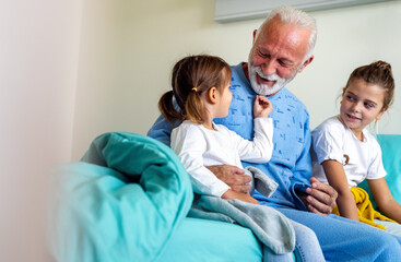 Obraz premium Happy recovering grandfather is visited by his grandchildren in the hospital.
