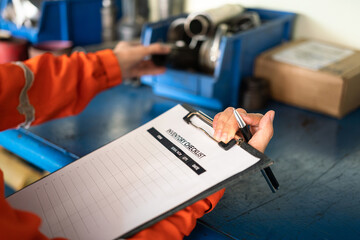 A worker is using pen to writing on inventory checklist form, with blurred background of storage...