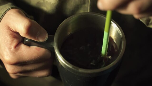 a soldier stirs sugar in a cup of tea close-up Field kitchen Preparing tea in a dugout Resting on duty A soldier warms himself with a hot drink at night during a break between combat operations
