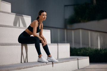 Fototapeta premium Sporty and fit woman sitting on the street, relaxing after nice workout session