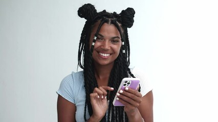 Beautiful multiethnic teenage girl with trendy hairstyle - dreadlocks, using mobile phone, sends a text message and smiles cutely, looking at camera, isolated on white background with ad copy space - Powered by Adobe
