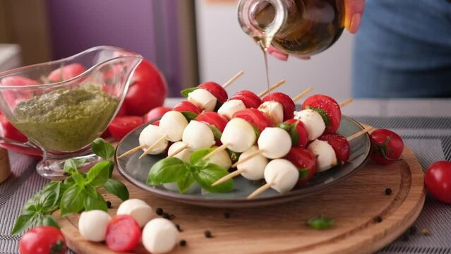 pouring olive oil on caprese canapes with cherry tomatoes and mozzarella cheese balls