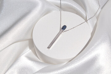 Silver pendant in the form of a match on a podium and white fabric background. Beautiful...