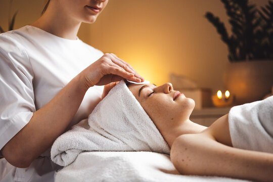 Close up of portrait of a woman lying with closed eyes having face cleaning by sponge in spa. Female beauty portrait. Girl facial treatment. Beauty skin. Skin