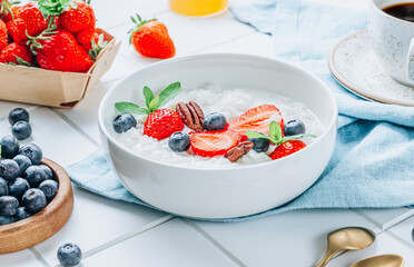 Homemade rice porridge or pudding with berry, nut, mint in a white bowl