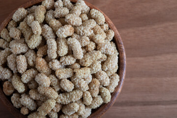 Bowl full of dried mulberry on a wooden background
