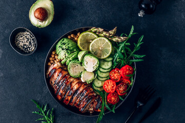 Healthy buddha bowl lunch with grilled chicken arugula, avocado, brussels sprouts, tomato, cucumber and chickpea