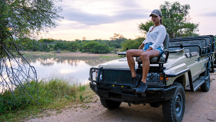 Asian women on a safari game drive in South Africa Kruger national park. women on safari. Tourist in a jeep looking sunset on safari - obrazy, fototapety, plakaty
