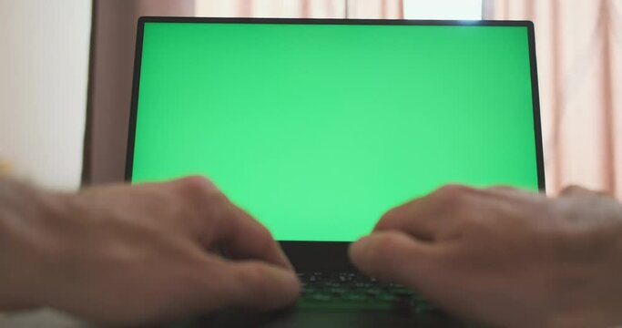 Male hands typing on laptop keyboard in front of reen screen. Concept of working at computer, home office, remote work, freelancing, writing a letter, working online. Front view, pov