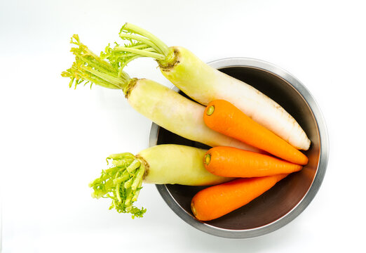 Organic carrots and white radishes in round shape stainless steel bowl, unpeeled carrots and radishes, top view image, isolated image on white background.