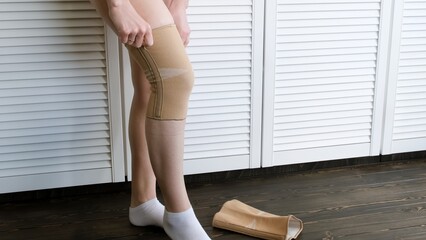 Flexible leg bandage. Young woman stands and puts an elastic band on her knees. Prevention and...