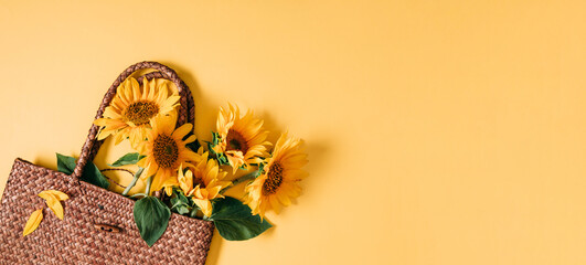 Summer or autumn background. Wicker bag with bouquet of sunflower flowers on yellow background. Flat lay, top view, copy space