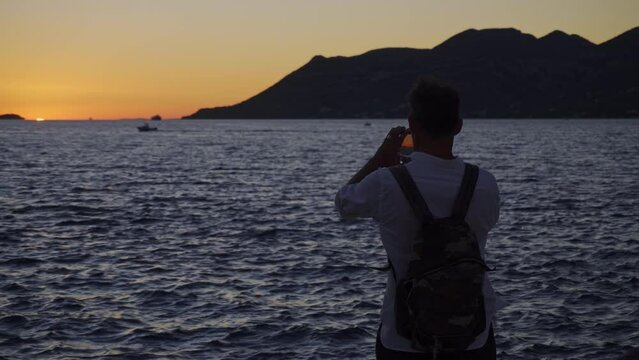 Backview Of A Man Taking Photos Of The Sea During Sunset. - medium, rear