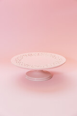 Small ceramic empty pink pedestal cake stand on a pastel pink table. Selective focus, copy space