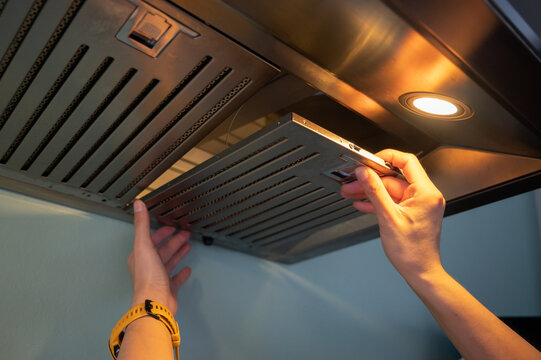 Woman hands trying to removing a filters from cooker hood for cleaning it. Clean your filters every two to three months, depending on your cooking habits.