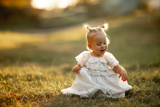 Happy little girl sits on the grass outdoors. Cute baby girl with blond hair is walking in park. Adorable kid play with grass. concept of happy childhood, games, fun. Family leisure. outdoor play