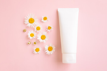 Mockup white squeeze bottle cosmetic tube, blooming medical chamomilles Daisy on pink background. Body cream, gel, skin care, sunscreen, moisturizer. Front top view, blank tube, template, flat lay.
