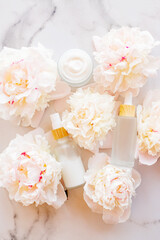 Concept skin care. A set of cosmetic products, creams and serum. Frosted glass bottles on white marble background with peony flowers. Rejuvenation and moisturizing. Flat lay.