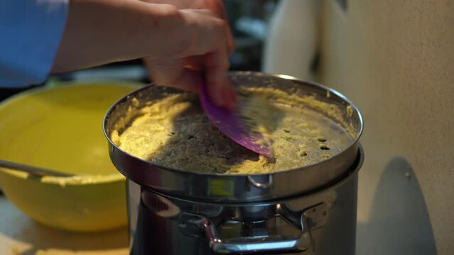 Hand Sliding Potato Dough On Spaetzle Maker Over A Pot. Making Bryndzove Halusky In The Kitchen. close up, side view