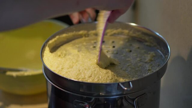 Hand Uses Plastic Spatula In Pressing Potato Dough Batter Onto Spaetzle Maker Over Pot With Boiling Water. close up