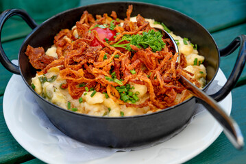 Pasta with cheese and fried onion, prepared in an black iron pan - rustic way to serve, on a green table