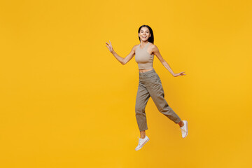 Fototapeta na wymiar Full body young satisfied cheerful smiling happy latin woman 30s she wearing basic beige tank shirt jump high like flying isolated on plain yellow backround studio portrait. People lifestyle concept.