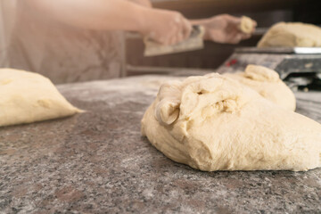 Close-up of elastic raw dough on a table sprinkled with flour, in the background a man cook weighs the dough by grams on a scale. Concept of baking, bakery