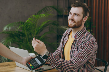 Young man he wear shirt hold wireless bank payment terminal smart watch process acquire credit card payment sit at table in coffee shop cafe rest in free time Freelance mobile office business concept