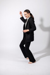 Happy with smile beautiful woman wearing classic black suit, white shirt and black tie dancing with bare feet on white studio background with copy space. Model with ponytail hairstyle