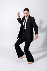 Happy with smile beautiful woman wearing classic black suit, white shirt and black tie dancing with bare feet on white studio background with copy space. Model with ponytail hairstyle
