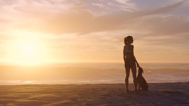R18-08-A-31. A female playing with her dog, throwing a ball at the beach during sunrise with copyspace. Young woman enjoying her day relaxing at the sea with her pet animal at sunrise in the morning.