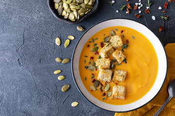 Autumn pumpkin vegetable cream soup in bowl served with seeds and crouton on black stone table top...