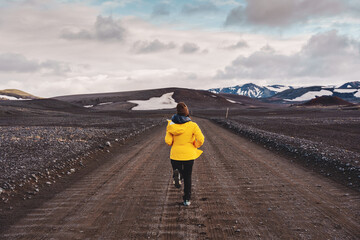 Asian woman in yellow jacket running on dirt road at highlands of iceland