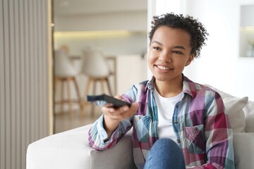 Happy biracial girl hold tv controller, watch movie or series, relax with television on sofa at home