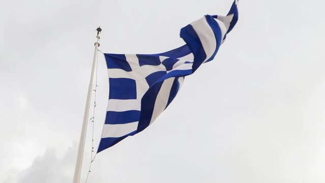 Waving Greek flag on a pole in a windy weather with grey sky