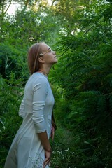 blonde in glasses and a white dress walks in the woods