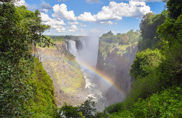 The iconic Victoria Falls, aka Mosi-Oa-Tunya waterfall, view from the Zimbabwe side with a rainbow. - obrazy, fototapety, plakaty