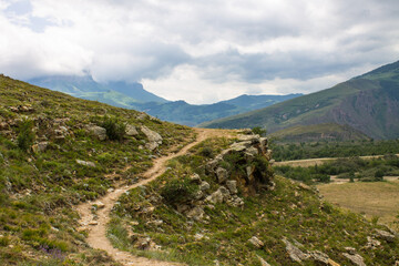 Fototapeta premium Dramatic landscape - steep cliffs and green hills with cloudy sky and fog on a summer day in the Elbrus region North Caucasus russia and soft blurred focus